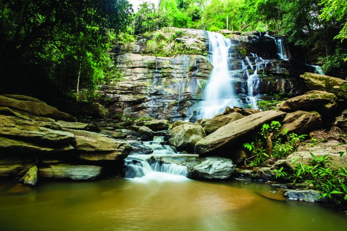 Fototapete Natürliche Landschaft Wasserfall zwischen Steinen und Bäumen