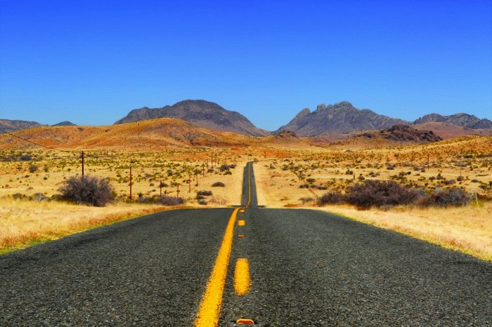 Fototapete Betonstraße, die durch die Mitte der Wüste führt