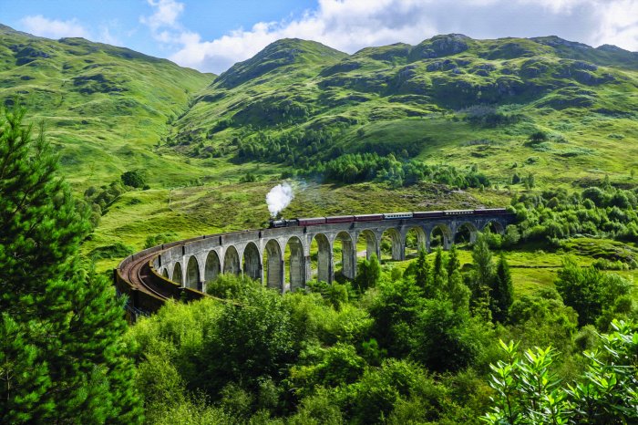 Fototapete Zug, der auf einer Brücke inmitten der Berge fährt