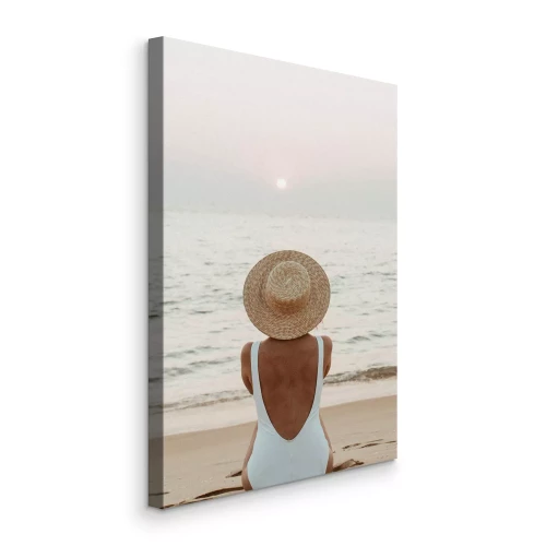 Bild Eine Frau mit Hut sitzt am Meer